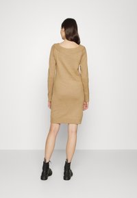 Vestito a maglia color marrone chiaro con scollatura a barchetta, maniche lunghe e orlo a coste, abbinato a stivali neri alla caviglia.