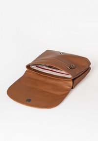Bruine leren tas met een afgeronde klep, voorzien van een zilveren drukknopsluiting. Het gevoerde interieur bevat een ritsvak met een rode accent.