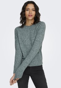 Pulover din material moale, texturat, de culoare gri, cu mâneci lungi, decolteu rotund și croială lejeră. Purtați cu pantaloni negri.