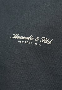Tecido preto com texto bordado em branco que diz "Abercrombie & Fitch" e "NEW YORK, N.Y." em uma fonte cursiva.