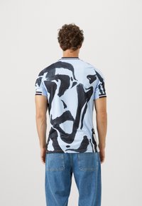 Krátky rukáv košele vyrobený z svetlomodrej látky s abstraktným čiernym vzorom. Zaoblený výstrih s kontrastnými pruhmi, voľný strih.