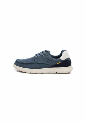 Zapatilla de lona azul con talón blanco y marino, diseño con cordones, parte superior texturizada y suela flexible y acolchada. Presenta una etiqueta de acento naranja.
