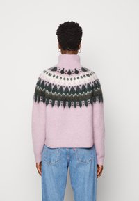 Dziany sweter z wysokim kołnierzem, różowym korpusem oraz wzorzystym karczkiem w ciemnozielonych, brązowych i białych odcieniach. Teksturowane wykończenie.