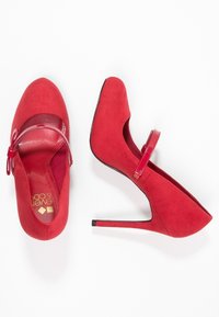 Red suede high-heeled shoes with a glossy strap and cutout design. Features a pointed toe and a slim stiletto heel. Smooth texture.
