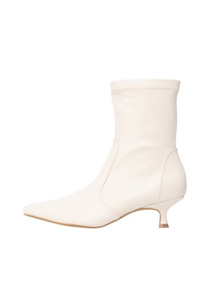Bottine blanche en matière lisse avec un bout pointu et un petit talon kitten bas. Design simple avec des détails de coutures discrètes.