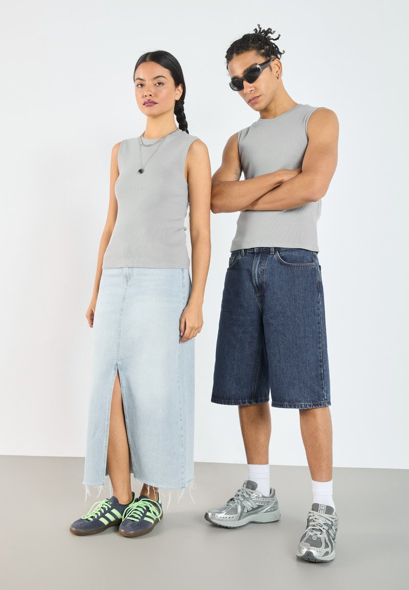Grå ribbestrikkede ermeløse topper, et lyst denim maxiskjørt med split, og mørk denimshorts; parret med sporty sko i grønn, grå og svart.
