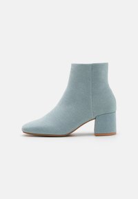 Bottine bleu clair en matériau textile. Dotée d'un bout pointu et d'un talon carré massif, avec une surface lisse et texturée.