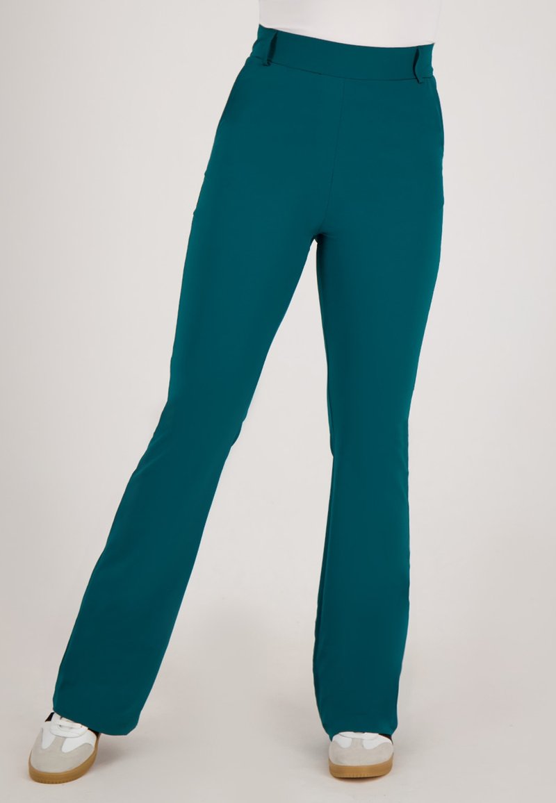 Teal, hoge taille rechte broek gedragen met witte sneakers, getoond van taille tot voeten tegen een effen achtergrond.