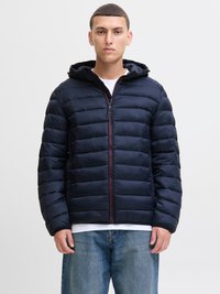 Giacca a vento trapuntata blu navy con cappuccio, dotata di zip frontale, tasche laterali e accenti rossi a contrasto lungo la zip.