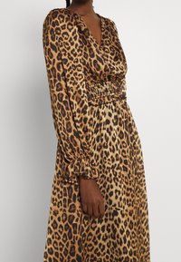 Leopardmönstrad maxiklänning med djup V-halsringning, smockad midja och långa ärmar med veckade manschetter i bruna och svarta nyanser.