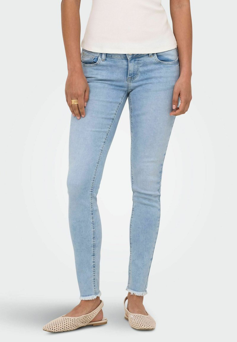 Jean slim bleu clair avec ourlets effilochés, porté avec des ballerines slingback tissées beige et un top blanc sans manches.