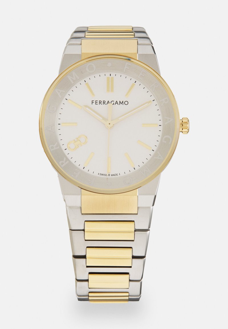 Relógio em aço inoxidável e tom de ouro com mostrador branco, marcado com ponteiros e índices dourados. Apresenta uma bracelete de metal sólido e gravação do logótipo.