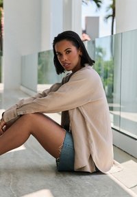 Light beige oversized button-up shirt with rolled sleeves paired with a distressed denim skirt. Smooth texture and relaxed fit.