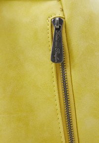 Żółta zamszowa część torby z srebrnym zamkiem błyskawicznym, posiadającym grawerowany uchwyt. Gładka faktura oraz staranne wykończenie szwu.