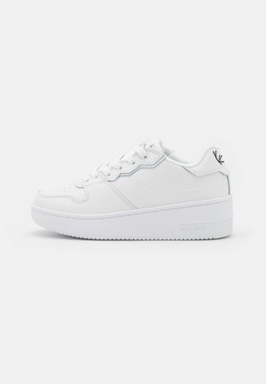 Zapatilla blanca de caña baja con suela gruesa, cordones delanteros, detalle sutil en relieve en el lateral y pequeño logo negro en la lengüeta del talón.