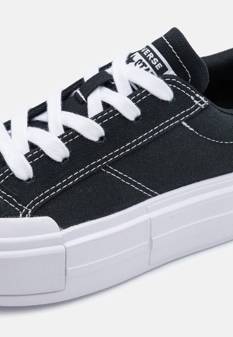 Scarpe da ginnastica in tela di colore grigio scuro con lacci bianchi, caratterizzate da una parte superiore testurizzata, cuciture a contrasto e una suola in gomma bianca spessa.