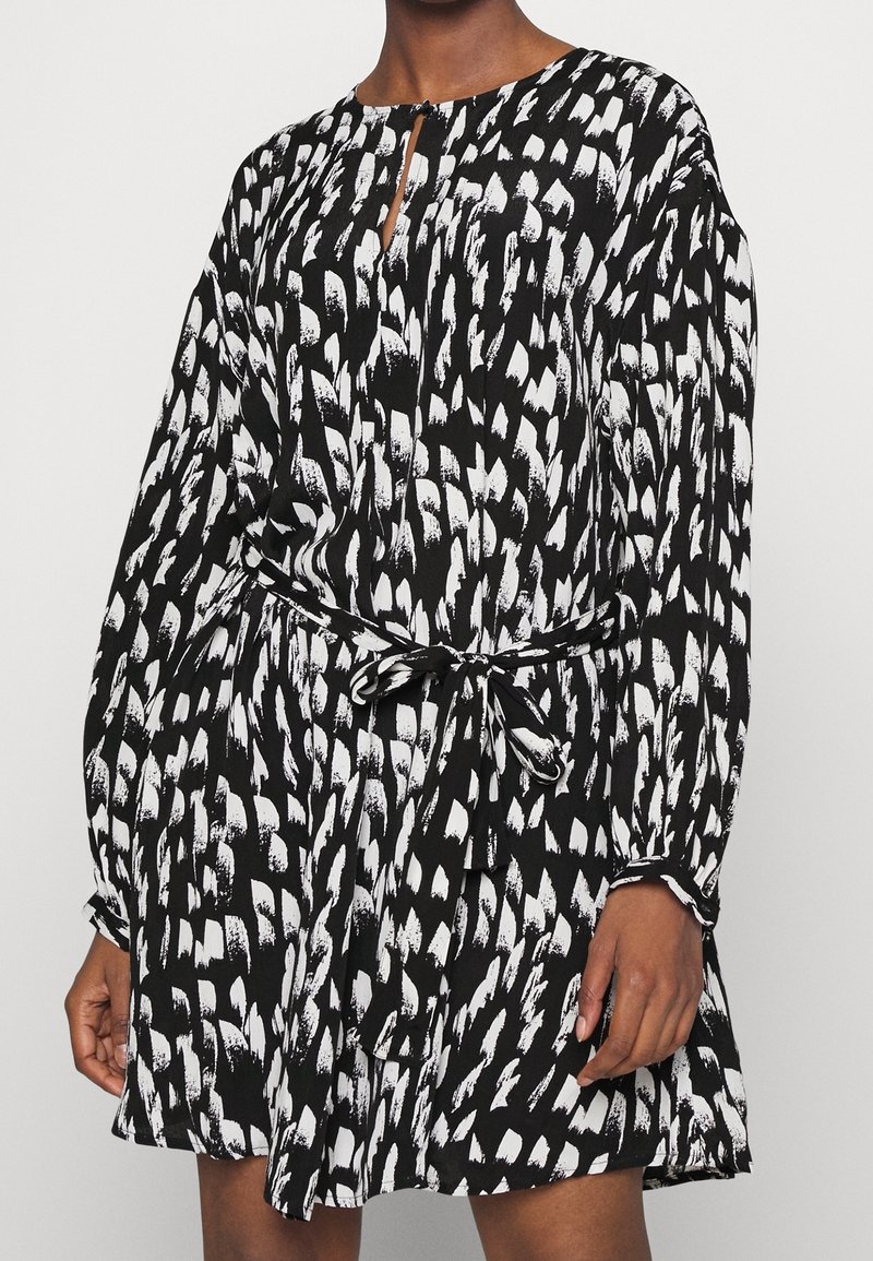 Schwarz-weißes Kleid mit langen Ärmeln, tailliertem Bund und Schlitzkragen. Hat ein abstraktes, malerisches Muster, das das gesamte Kleid ziert.