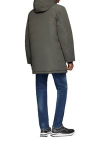 Gevoerde donkergrijze parka met een capuchon, met een rechte snit. Gecombineerd met blauwe denim jeans en zwarte sportschoenen met witte accenten.