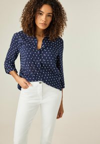 Camisa de botones azul marino con patrones rectangulares blancos, mangas largas remangadas, combinada con pantalones ajustados blancos. Tejido suave y corte relajado.