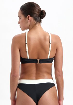 Top bikini nero con spalline crema e dettagli dorati, caratterizzato da spalline regolabili e chiusura posteriore sicura; con pantaloni bikini neri coordinati.