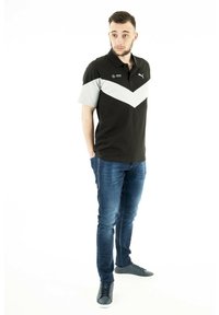 Zwarte en grijze polo met een chevron-ontwerp, voorzien van een kraag en logo-accenten, gecombineerd met blauwe jeans en grijze sneakers.