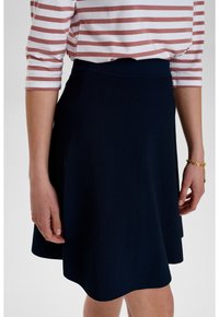 Laivastonsininen skeittihame, jonka muoto on levenevä ja joka on valmistettu kevyestä kankaasta. Hameessa on sileä vyötärö ja se ulottuu polven ylle.