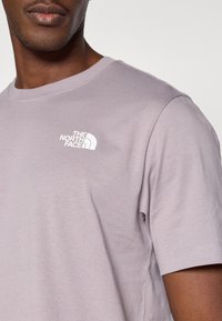 Λιλά κοντομάνικη μπλούζα από βαμβάκι με στρογγυλή λαιμόκοψη, με μικρό λευκό λογότυπο στο αριστερό στήθος. Λείο ύφασμα.