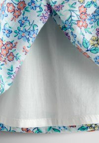 Tela ligera con estampado floral que presenta pequeñas flores naranjas, rosas y azules sobre un fondo blanco. Bordes rematados con un interior blanco liso.