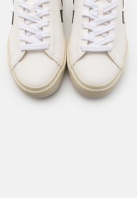 Weiße Leder-Sneaker mit flachen weißen Schnürsenkeln, runder Zehenpartie und dezenten schwarzen Akzenten an den Seiten. Strukturierte Gummisohlen.