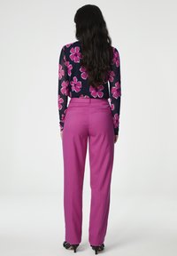 Langarm bloemenblouse met een marineblauwe achtergrond, gecombineerd met hoge taille roze broeken, voorzien van een taps toelopende pijp en achterzakken.