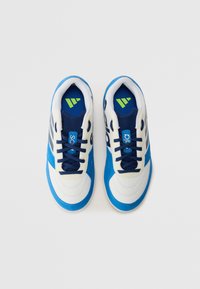 Zapatillas deportivas en azul y blanco con parte superior de malla, lengüeta acolchada y cordones. Cuenta con un logo verde en la plantilla y franjas laterales. Textura suave.