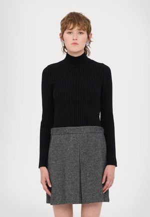 Maglione nero a coste con colletto alto abbinato a una gonna in tweed grigia con pieghe a scatola. I materiali sono maglia e tessuto testurizzato.