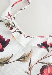 Haut sans manches à motif floral avec un tissu texturé blanc, mettant en avant des fleurs multicolores dans des teintes de rouge, rose et vert.