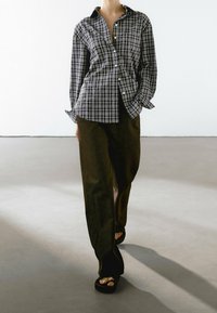 Czarna i biała koszula w kratę z długim rękawem, zestawiona z ciemnobrązowymi spodniami o szerokich nogawkach i czarnymi sandałami na platformie.