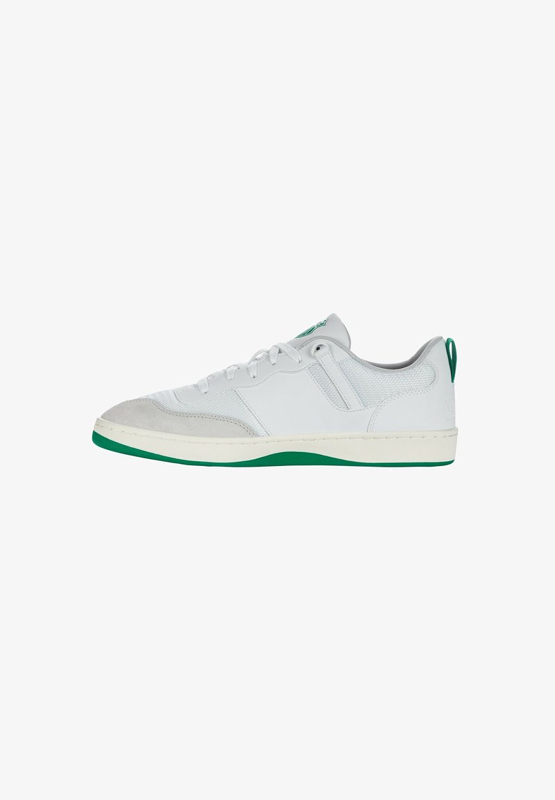 Zapatilla blanca con parte superior de ante y textil, acentos verdes en la suela y el talón, cordones planos, detalles cosidos y un diseño de corte bajo.