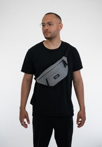 Borsa a tracolla grigia realizzata in tessuto resistente, con un compartimento principale con zip, una tasca frontale con zip e una cintura regolabile.