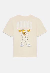 Cremfarbener T-Shirt mit einem Grafikdesign eines Charakters in einem weißen Trainingsanzug, mit dem Text "ADIDAS" darüber in fetten weißen Buchstaben.