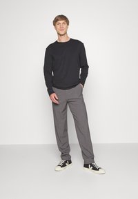 Langärmliges schwarzes Shirt, graue maßgeschneiderte Hosen und schwarze Sneakers mit weißen Sohlen. Einfaches Design mit lockerer Passform und glatter Textur.