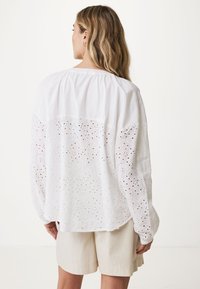 Vit bomullsskjorta med intrikata spetsdetaljer, långa ärmar och en avslappnad passform. Slät textur, rundad nederkant och ryggparti med design.