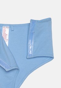 Biancheria intima in cotone blu chiaro con una texture liscia, dotata di un'etichetta con testo cautelativo e cuciture decorative lungo le cuciture.