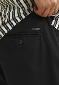 Ručně zasunutá pruhovaná košile do černých kalhot s zadní kapsou na knoflíček a malou značkovou etiketou Jack & Jones.