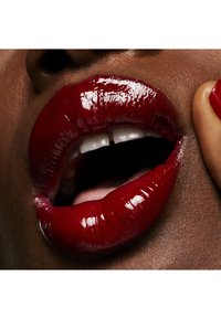 Lèvres rouges brillantes avec une brillance distincte, montrant une forme pleine et de légères variations de texture, sur des tons de peau plus foncés. Bouche ouverte révélant des dents blanches.