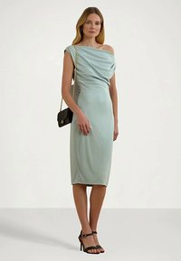 Vestido justo de cor azul claro com decote drapeado fora dos ombros e bainha até ao joelho. Tecido suave e detalhes de modelagem subtis. Bolsa preta e saltos altos.