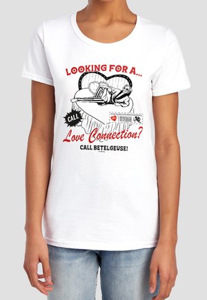 Woman wearing white t-shirt with vintage-style cartoon of man on heart-shaped bed and text about finding love, calling Betelgeuse.