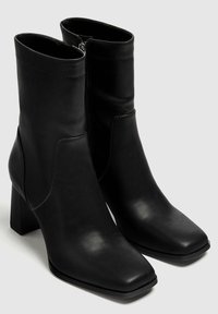 Bottes noires à hauteur de la cheville en cuir synthétique, dotées d'un bout carré, d'une fermeture zippée latérale et d'un talon bloc à motif texturé.