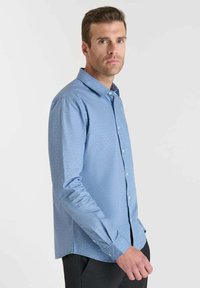 Lichtblauwe langarmshirt met een subtiel stippenpatroon, knoopsluiting bij de kraag en manchetten. De stof lijkt glad en gestructureerd.