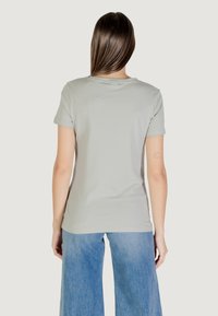 T-shirt grigio chiaro a maniche corte con colletto rotondo, realizzato in un materiale morbido. Il modello lo indossa con jeans a gamba larga blu chiaro, visto da dietro.