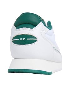 Sneaker in pelle bianca con dettagli verdi, caratterizzato da un tallone imbottito, design testurizzato e un piccolo dettaglio "1973" sul retro.