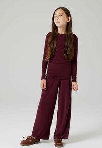 Maglia a maniche lunghe color marrone bordeaux abbinata a pantaloni ampi marrone bordeaux, realizzati in un tessuto morbido. Include scarpe robuste marroni con lacci e suole testurizzate.