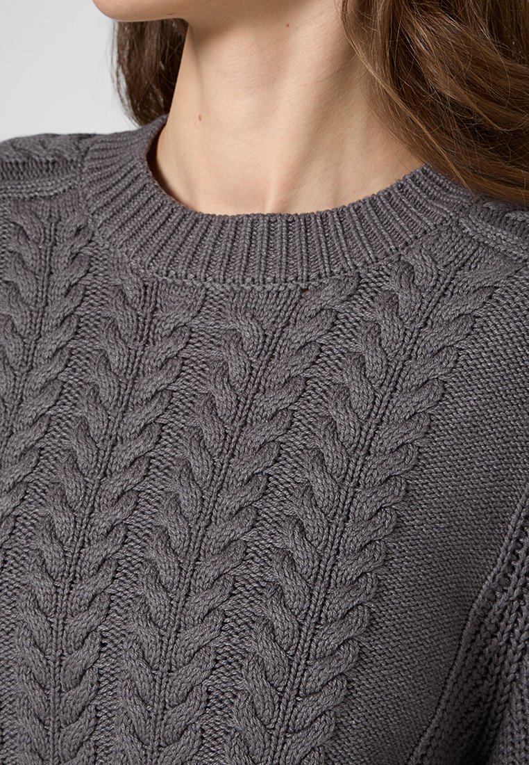 Grauer Strickpullover mit geripptem Rundhalsausschnitt, strukturierten Kabelmustern und weichem Finish. Nahaufnahme des Ausschnitts und der Stoffdetails.